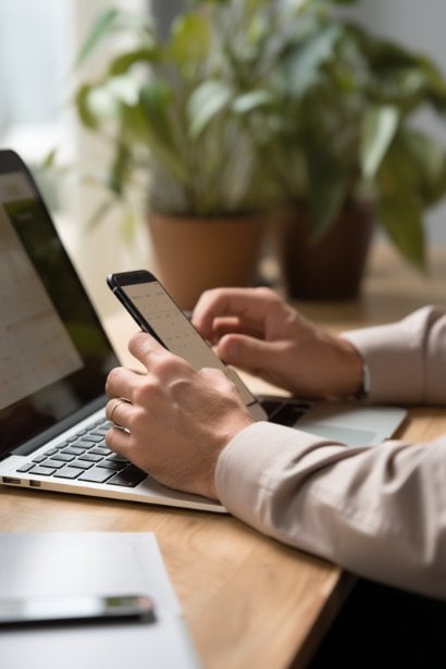 A close-up of a male's hands typing on a keyboard with a smartphone displaying a calendar beside him. The individual's expression isn't visible, but the focus is on the act of crafting a response and scheduling, reflecting the meticulous nature of responding to an interview request.