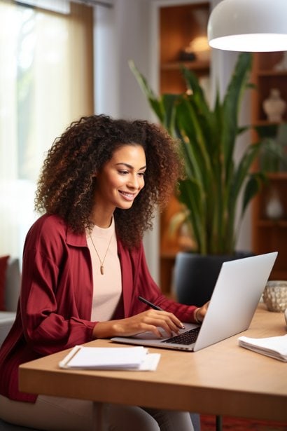 A young professional (female) is seen reviewing her resume on a laptop in a bright home office setting. She has a look of satisfaction and confidence, reflecting the empowerment that comes with asserting her identity on her professional documents.