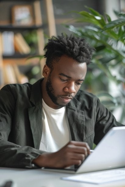 A young male professional at a clean, organized workspace, looking at a digital tablet. He's making notes with a focused expression, embodying the strategic planning and goal-setting process for improvement.