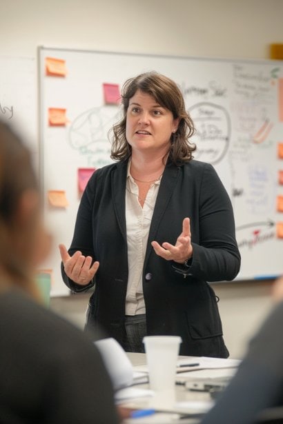 A female professional, looking resourceful and proactive, leading a crisis management meeting with a calm and composed demeanor. The meeting room has a whiteboard with strategies outlined, symbolizing her adaptability in navigating workplace challenges.