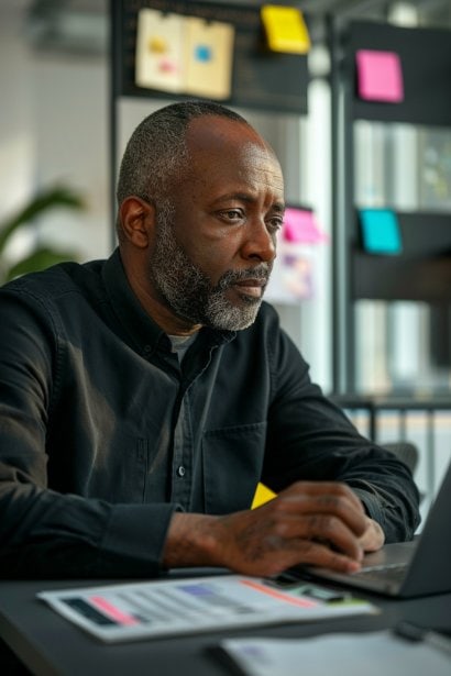A focused male professional, sitting in a modern office, surrounded by notes and a digital tablet displaying a calendar and checklist. His expression is one of deep concentration, highlighting the importance of thorough preparation for a successful meeting.