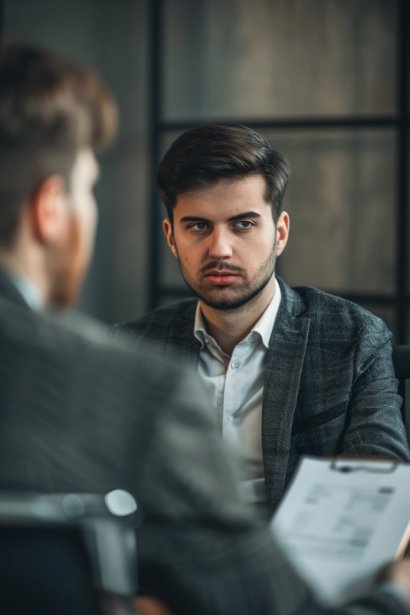 A photo illustrating a serious yet calm private conversation between a young male professional and his boss in the boss's office. The employee is shown presenting his concerns using documents to provide evidence, maintaining a professional demeanor. The boss listens attentively, nodding, symbolizing a receptive and thoughtful management response.