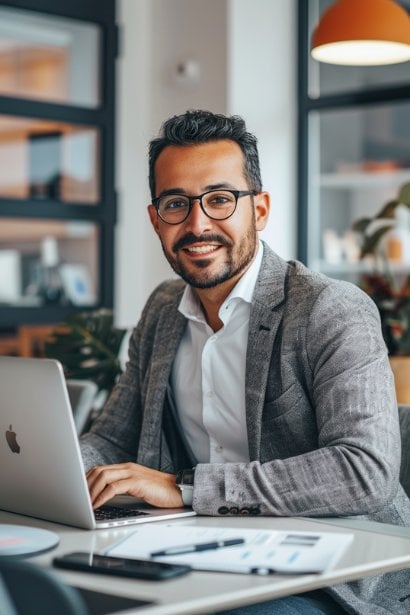 A male professional in his early 30s, looking upbeat and motivated, working on a presentation at his laptop in a bright, modern office. Reflecting his dedication to quantifying his impact and demonstrating career achievements.