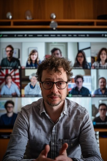 A virtual meeting screen showing a male interviewer in the central frame, looking attentive and nodding, as he conducts a virtual group interview. Surrounding his frame are smaller frames, each with a candidate speaking or waiting their turn. The atmosphere is professional and dynamic, with each participant showing determination and readiness to engage.