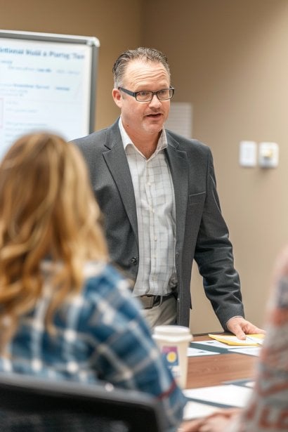 A senior male manager, showing a commanding yet approachable demeanor, conducting a training session for a small group of staff on inclusive policies. The setting is a conference room, and the manager is actively engaging with the attendees, illustrating proactive management practices.